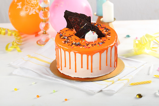 Orange Drip Cake light background banner with party decor. Copy space. Celebration concept. Trendy Drip Cake. Selective focus.