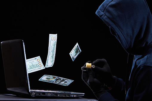 Criminal steals money from bank. Hacker in hood working at laptop and open lock with key. An anonymous hack password personal data.