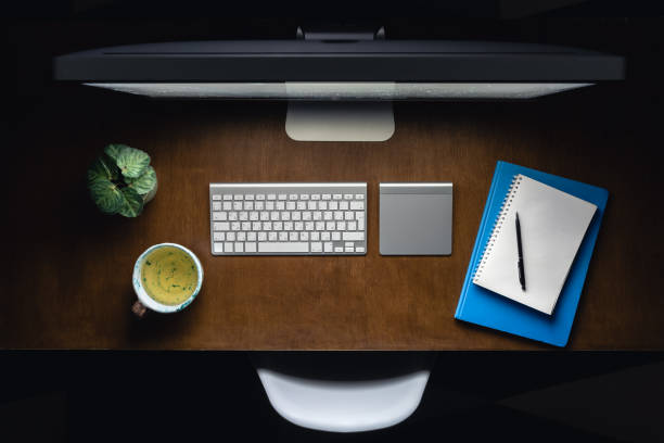Computer, notepads and a cup of tea on the desktop at night, top view. Workplace in the office late at night. Night work concept.