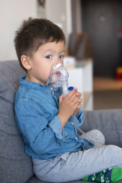 young child using a inhalation nebulizer at home - tubing child oxygen mask medical oxygen equipment fotografías e imágenes de stock