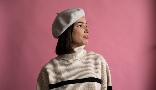 French style. Portrait of a smiling woman dressed in beret standing and looking away isolated over pink background