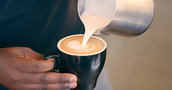 Hand, art and pouring milk for espresso at cafe in morning to prepare, breakfast in startup business. Closeup, black person and cup for coffee with creativity in morning for customer and professional