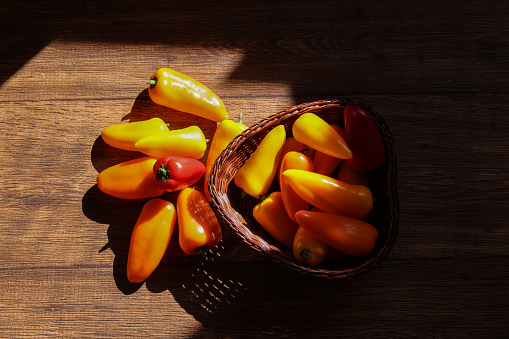 Various color of sweet peppers in a basket on a wooden table.