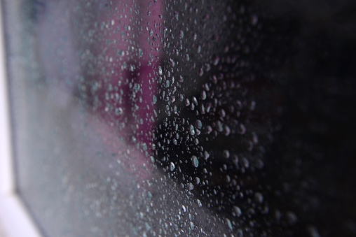 Raindrops on the window glass close-up with Red light. Night light reflection on wet glass. Droplet background texture. Dark background