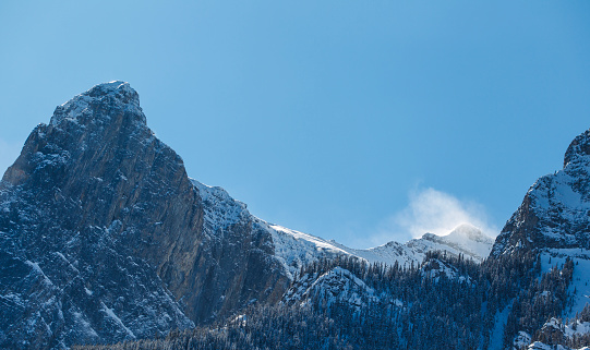 The wind blows the snow off a mountain ridge near Canmore, Alberta, Canada in the wintertime.