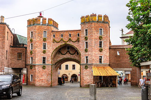 Landshut, Germany - July 24, 2023: Restored medieval town gate Landtor in old town. Old red brick gate and people walking along streets on rainy summer day, Landshut, Germany
