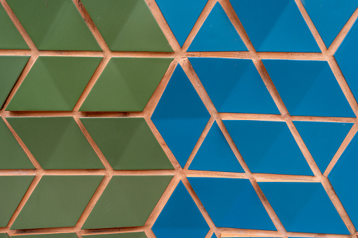 Geometric pattern composed of green and blue triangular tiles. Neatly arranged pieces forming large design. Thin terracotta-colored lines separating it. High quality photo