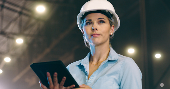 Woman, tablet and warehouse for construction with helmet, ideas or inspection at building project. Architect, contractor and property developer on touchscreen for thinking, communication and industry