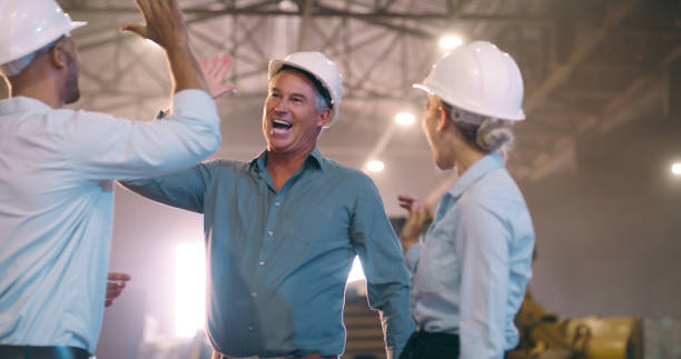 hombres, mujeres y choca los cinco en el almacén con la construcción, la planificación y el equipo con la celebración de los goles. personas, contratistas y vítores para el promotor inmobiliario con éxito en la fábrica con arquitectura - cheering business three people teamwork fotografías e imágenes de stock