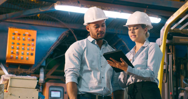Business people, cooperation and tablet for electrical engineering, typing and planning in a workshop. Helmet, manager and employee with technology and internet with inspection and online software