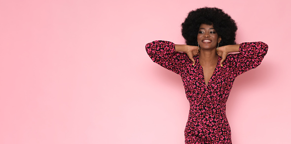 Pretty black woman in a floral dress on a pink background.