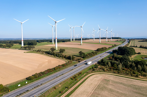 Aerial view of a large wind power plant in a summer patchwork landscape with a rural highway.