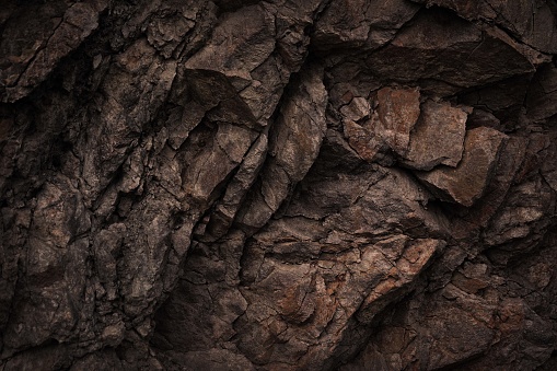 Black dark brown gray stone rock granite basalt texture background. Mountains surface. Close-up. Cracked broken crumbled.