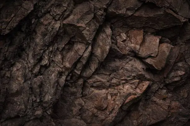 Photo of Black dark brown gray stone rock granite basalt texture background. Mountains surface. Close-up. Cracked broken crumbled.