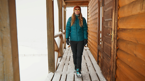 Young woman on publicly owned log cabin deck prepares to go out in snow storm