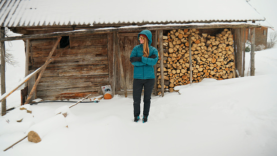Young woman outside log cabin deck pauses by wood pile