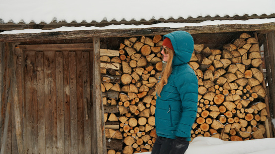 Young woman outside log cabin deck pauses by wood pile