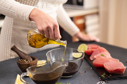 Woman pours olive oil into glass bowl with soy sauce making marinade to marinate Pieces of Fresh tuna Fish fillet.