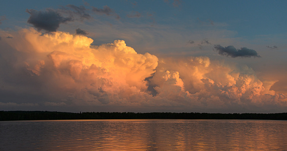 Orange and white storm clouds on horizon over northern Minnesota lake at sunset, reflection on lake