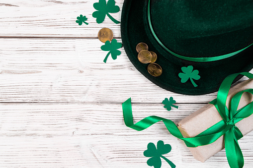 Background for St. Patrick's Day. Leprechaun hat, gold coins and clover shamrock on white wooden background. Good luck symbols. Place for text.
