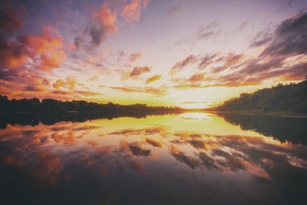 Sunrise or sunset on a lake or river with dramatic cloudy sky reflection in the water in spring. Springtime rural landscape. Aesthetics of vintage film.