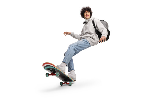 Cool young man with headphones and backpack riding a skateboard isolated on white background