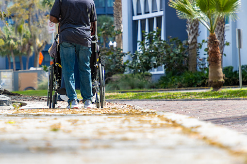 A nurse pushes an elderly person in a wheelchair down the sidewalk.