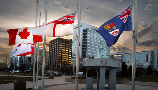 American and Canadian flags, showing the full stars and stripes and maple leaf respectively, on silver flagpoles blowing in the wind against a backdrop of snow covered mountains and forest trees