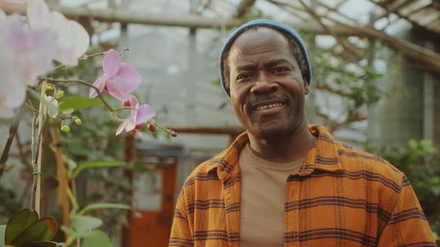 Portrait of Happy Black Man beside Orchids in Flower Greenhouse