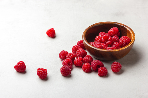 Fresh raspberries in a wooden bowl on a light grey background. Red berries.