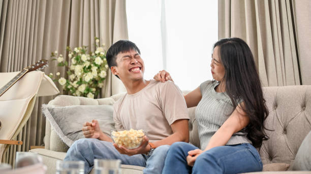 istock A joyful Asian couple is laughing at jokes and enjoying popcorn while watching television together. 2062014871