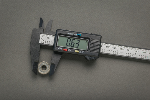 Measuring the nut with an electronic vernier caliper on a gray background. A tool for accurate measurement of dimensions.