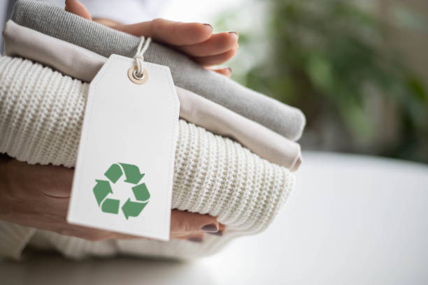 istock Woman's hands hold a stack of clean neat knitted clothes with a label with a recycling sign. 2062042253