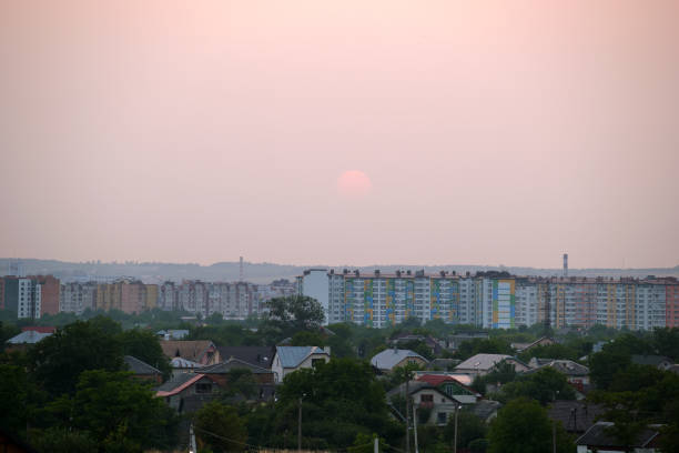 Evening landscape with bright setting sun over distant city high rise buildings at sunset.