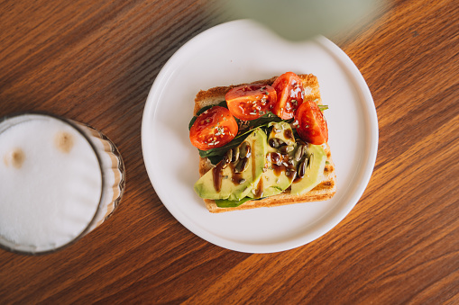 Avocado and tomato toast on a white plate with coffee.