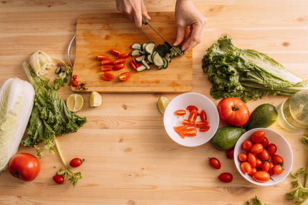 istock Lady cuts cherry tomatoes and cucumbers on a wooden table on which there are fresh vegetables 2062070591