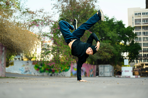 Shot of young male hip hop dancer in stylish clothes performing a handstand in city street.