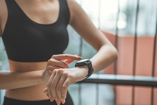 Close-up image of woman checking her smartwatch and counting calories burned during a workout session, Happy runner checking heart rate on wristwatch after exercising outdoors.