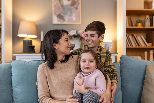 Mother shares a tender moment with her children. With her daughter and son by her side on the sofa. Their smiles speak volumes of the joy they find in each other's company