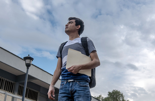 Male student holding a file and looking up at the sky