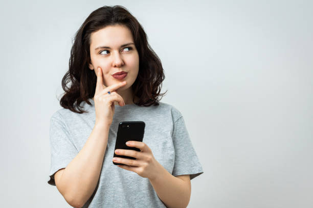 istock Beautiful young girl with phone looking aside 2062417102