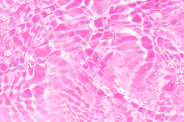Water surface. Pink water waves on the surface ripples blurred. Transparent pink colored clear calm water surface texture with splash and bubbles. Purple water waves with shining patterns. Caustics.