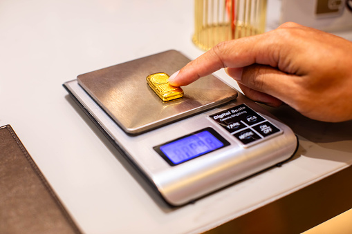 Selective focus to hand of a gold shop employee is  weighing gold bar on a digital scale.