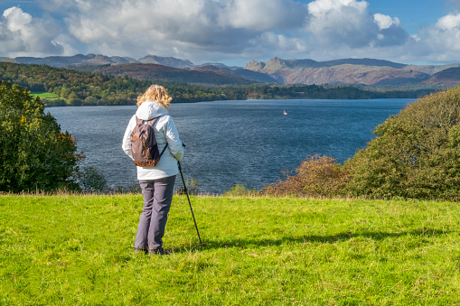 A senior female hiker with walking pole on Queen Adelaide's Hill overlooking Lake Windermere in the English Lake District, Cumbrias, North West England, UK.