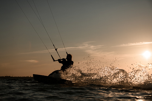 Female wakeboarder rides a wakeboard, holding on tightly to a comfortable handle on the cable against the background of the sunset, splashes flying to the side of the board