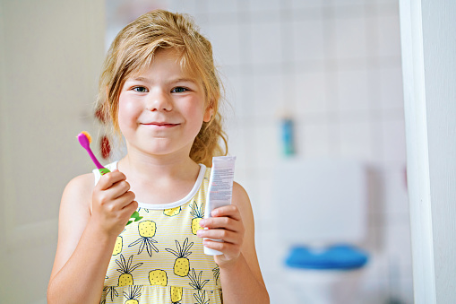 Cute little girl with a toothbrush and toothpaste in her hands cleans her teeth and smiles. Happy preschool child brushing first teeth