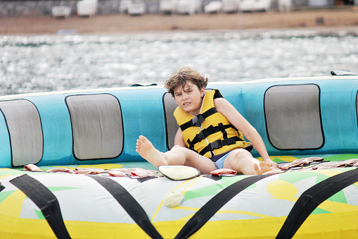 Young boy exudes joy while riding an inflatable tube towed by a boat in the ocean. Happy school child having fun in adventure water park on the sea