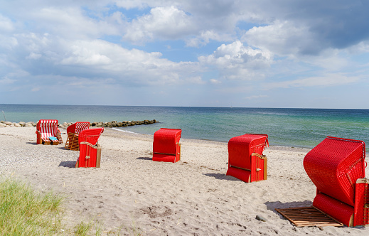 Traditional German roofed wicker beach chairs on the beach of Baltic Sea. Beach with red chairs on stormy sunny day. Ostsee.