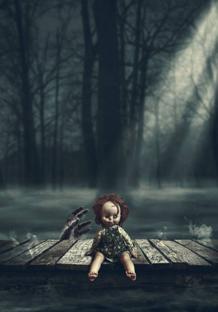 Creepy doll on a wooden deck at night, a zombie hand is rising behind her: horror and mystery concept