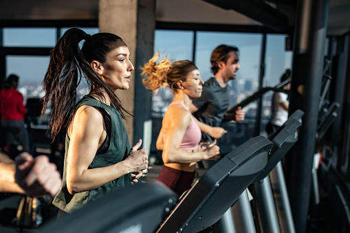 Determined athletic woman jogging on treadmill among other athletes in a gym.